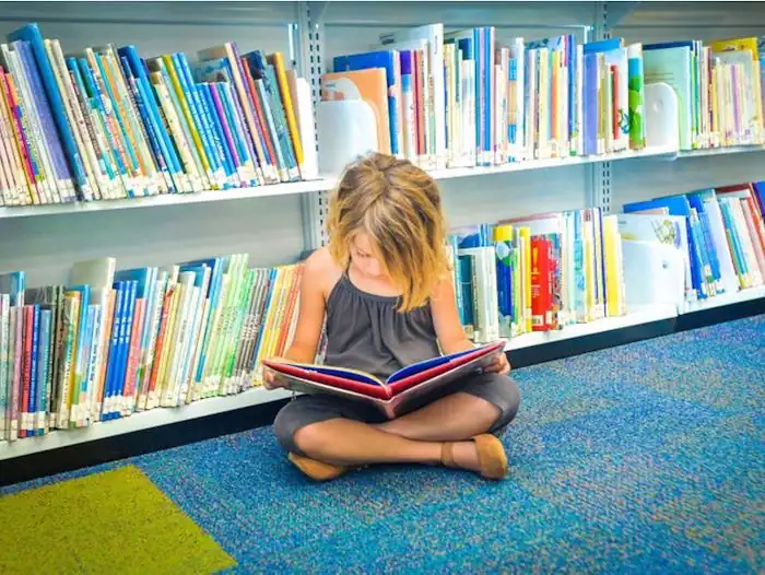 girl sitting down in library reading a book