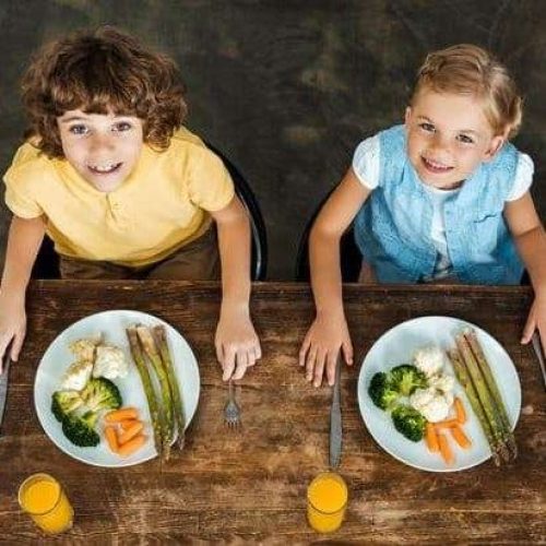 two children sitting at a table with a healthy dinner in front of them