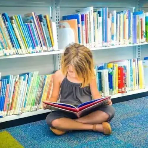 child sitting on the floor of a library while reading a book