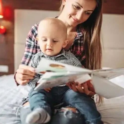 mother with baby reading a book while sitting on a bed.